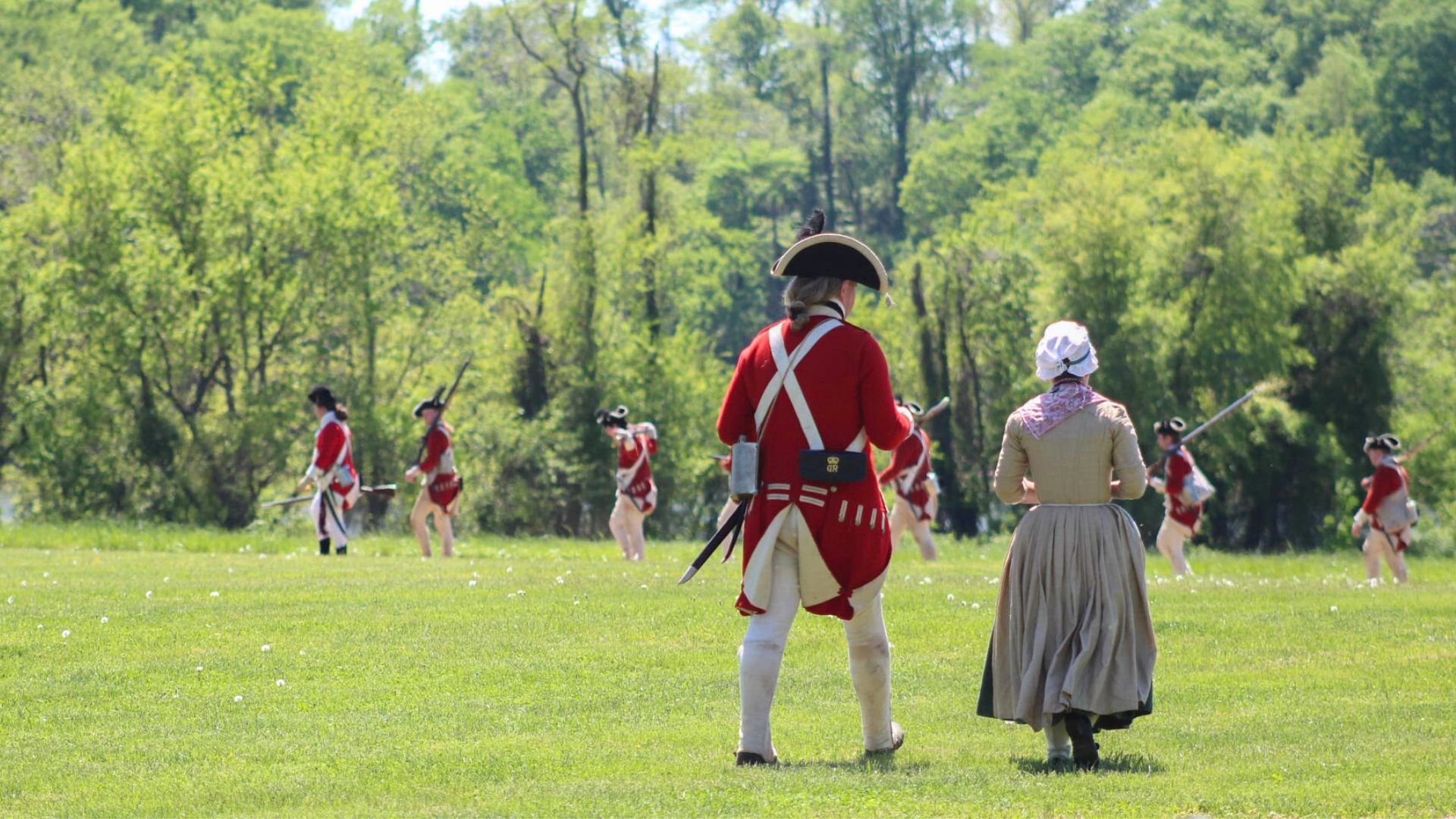 On patrol, 18th-century soldiers walk alongside a camp follower in a living history photography scene.