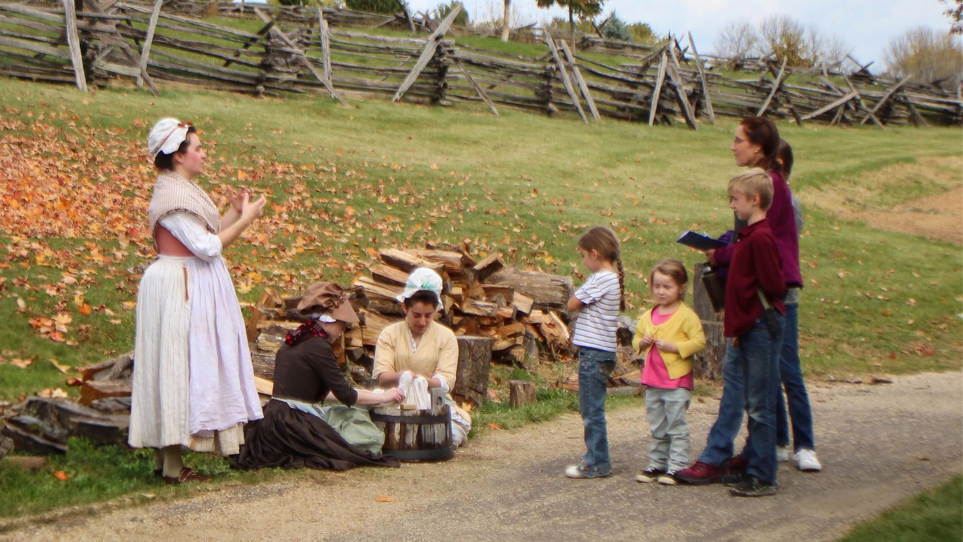 In a living history photography scene, a laundress reenactor speaks with a family and their young children.