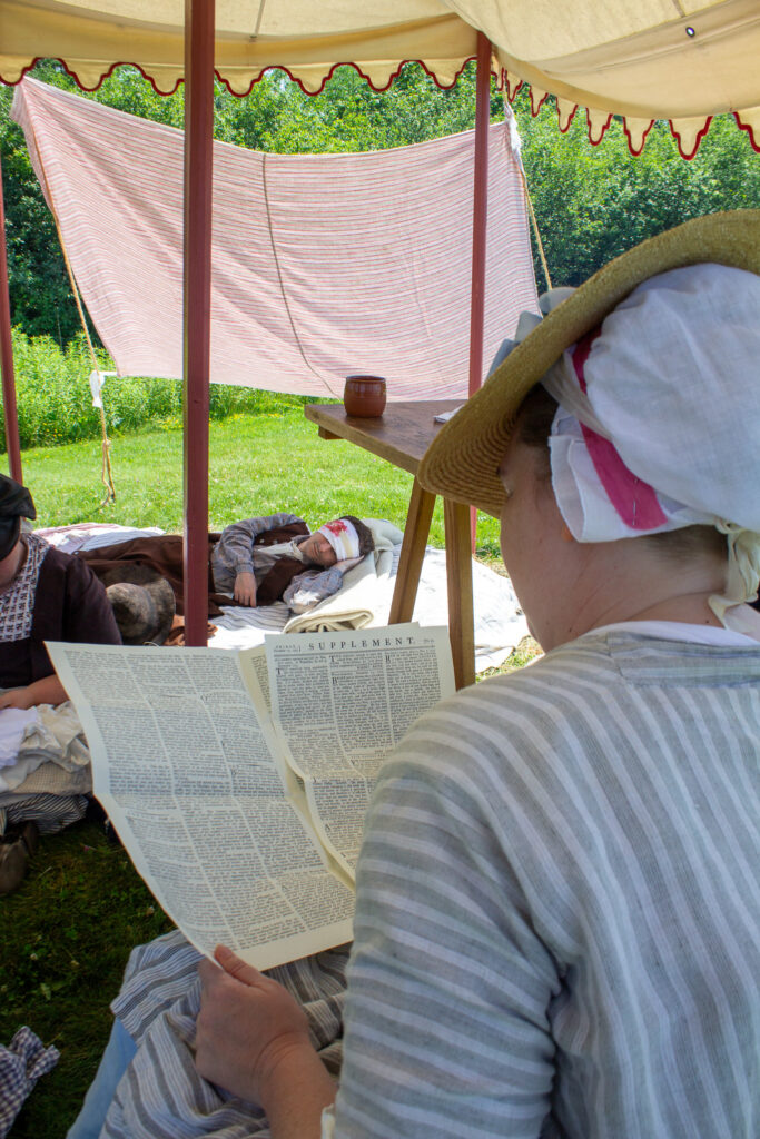 A camp follower reads a newspaper to a patient at the flying hospital, Fort Ticonderoga, Ticonderoga, NY. 2026.